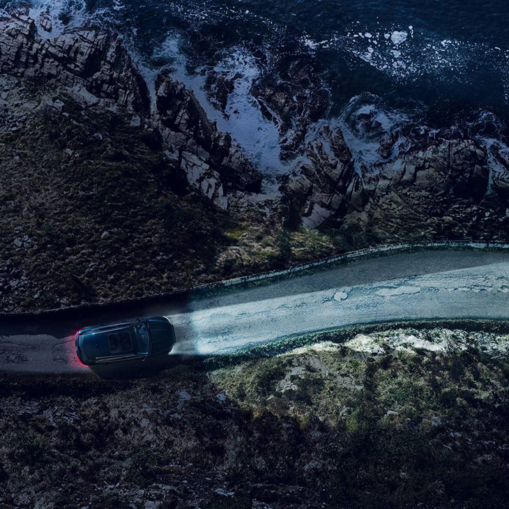 Audi e-tron auf einer dunklen Straße in den Bergen mit eingeschaltetem Fernlicht