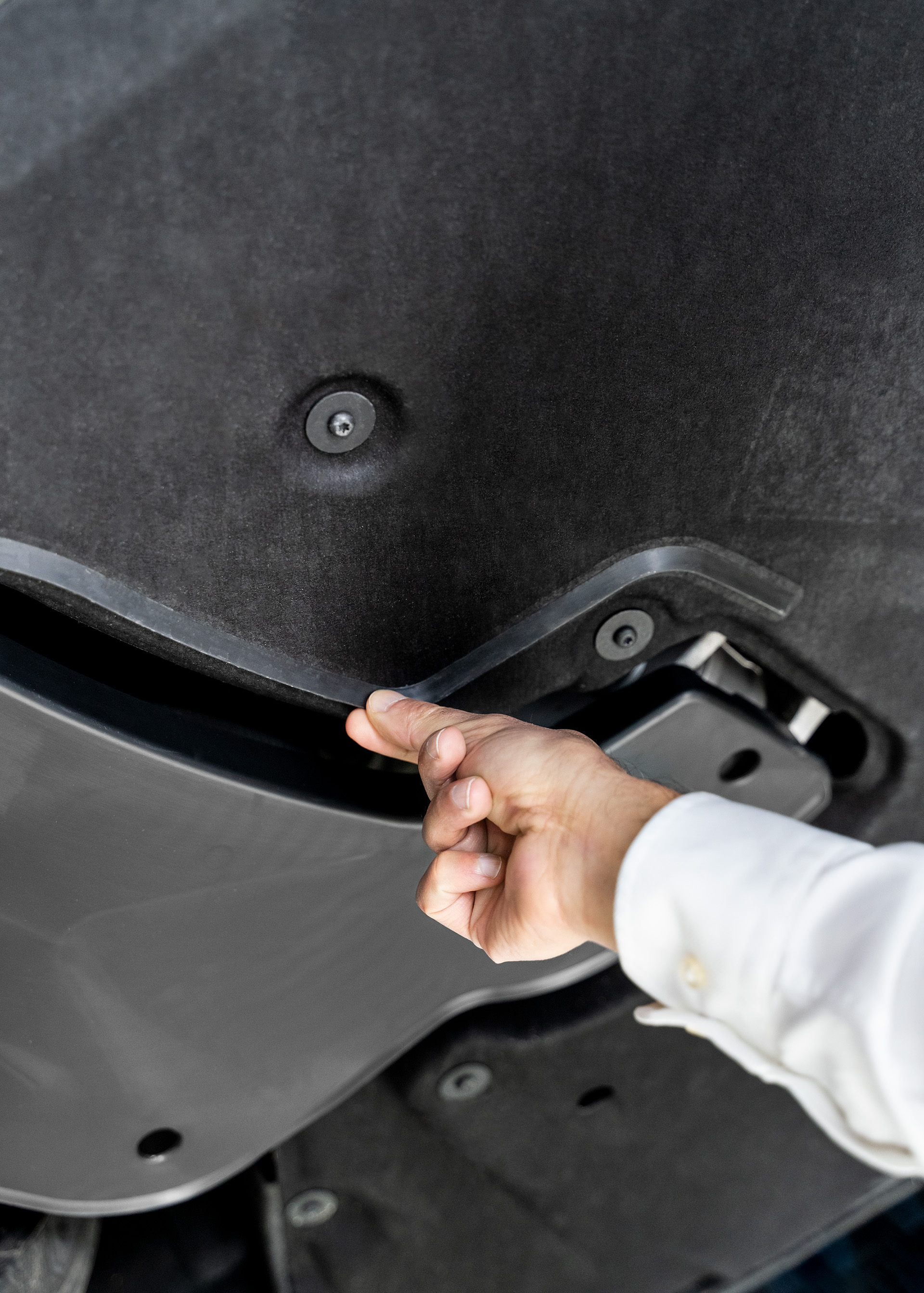 Eine Hand berührt eine Kunststofflippe am Fahrzeug-Unterboden. 