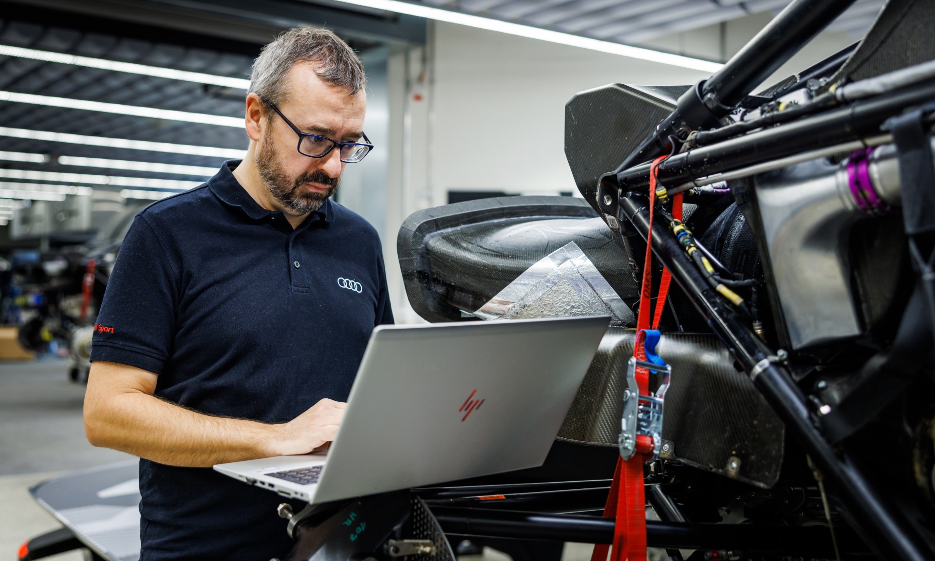 Arnau Niubó Bosch en situation de travail sur ordinateur à côté de l'Audi RS Q e-tron démontée. 